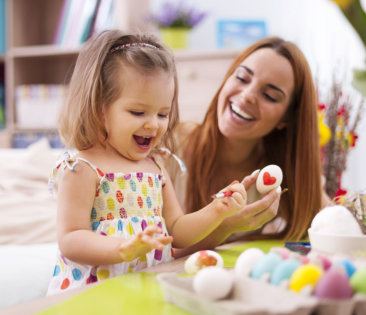 happy kid painting something on an egg with a middle aged woman